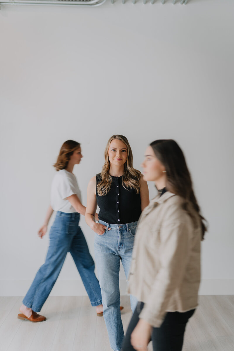 Megan standing in front of a white wall with her team members walking around her