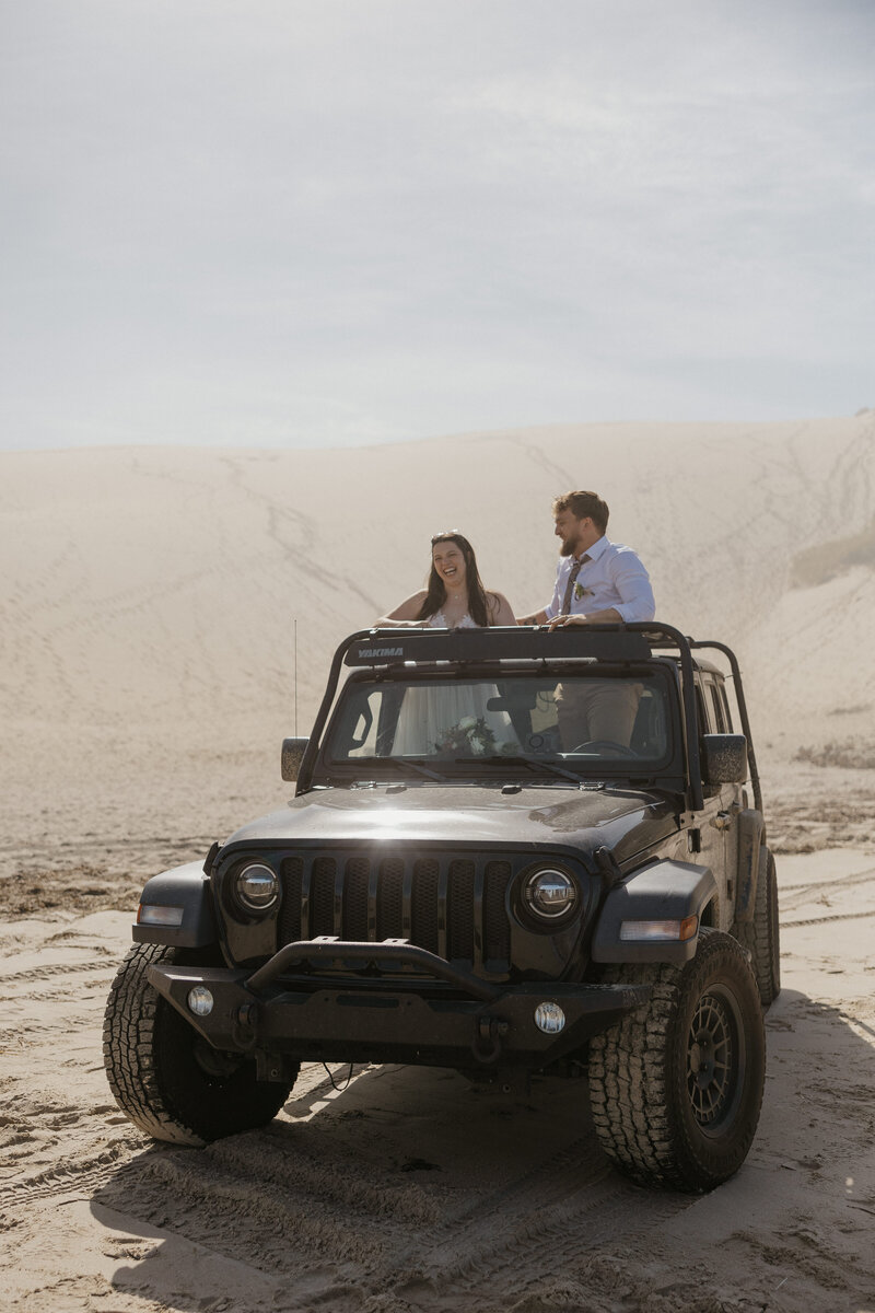 Couple laughing in their Jeep during their Oregon Coast elopement in the sand dunes