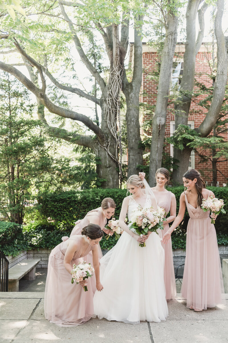 Bride being supported by her bridesmaids outdoors at Meadow Brook Hall—capturing calm, candid moments of connection and joy.