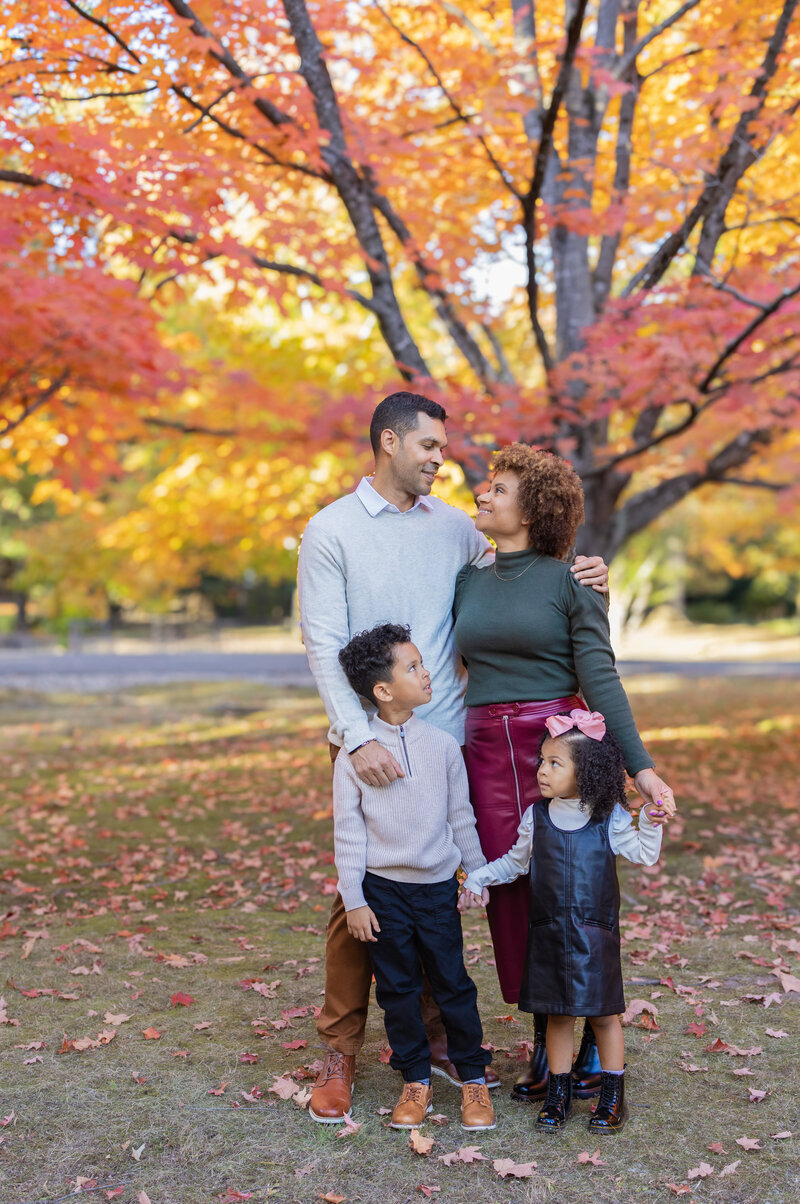 Family smiling during a portrait session beneath vibrant orange maple trees during fall season in near Paramus, NJ