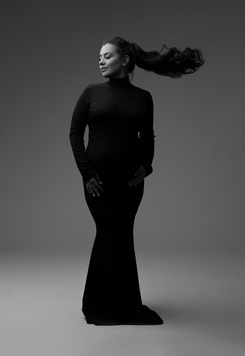 a pregnant woman in a long black dress with a pony tail during a maternity photoshoot