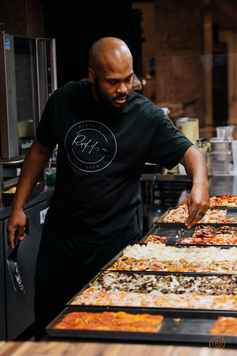 A man uses a spatula to remove a slice of pizza from the metal tray in a warmly lit restaurant. 
