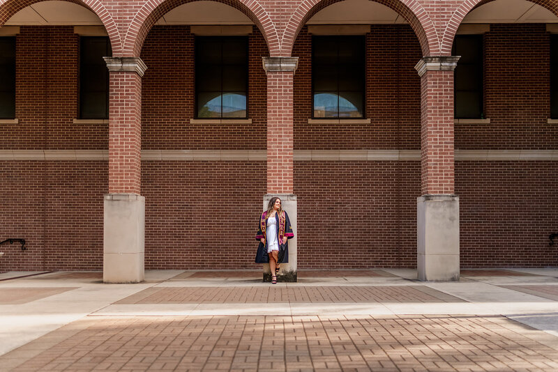 College graduate girl in white dress standing in front of purple door on Tarleton State University campus

