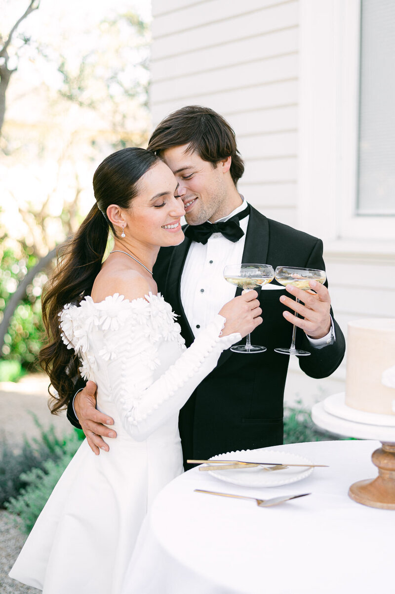 Chic bride and groom hold champagne coups and embrace