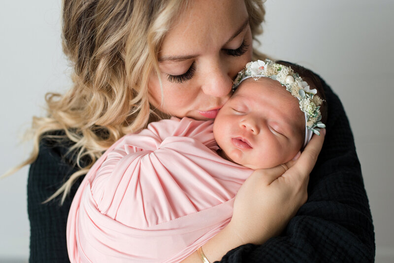 Sleeping baby girl gets kissed by Mom during newborn pic session.