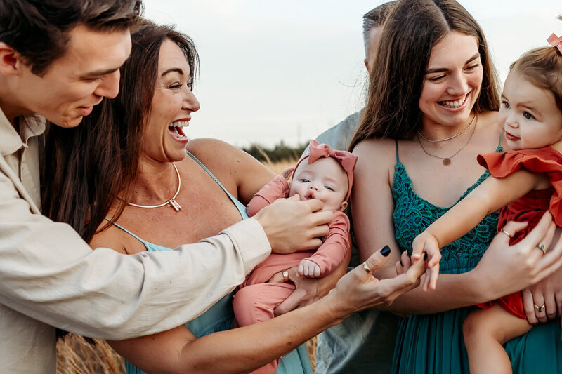 Family laughing and playing with babies in a grassy field