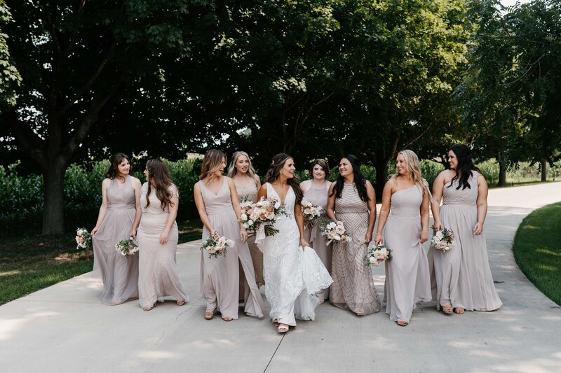 A bride and her bridesmaids in mismatched dresses walking together and laughing.