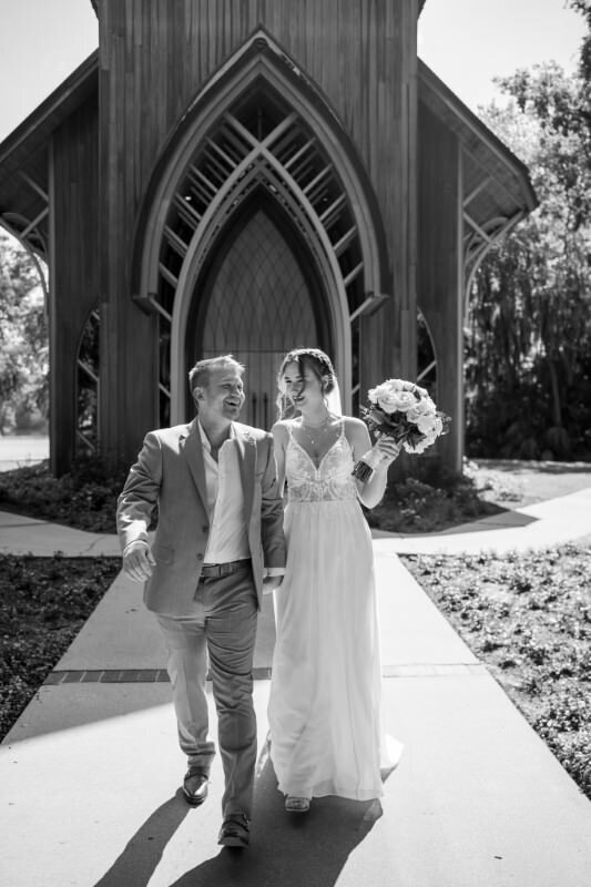 groom in a suit and a bride in a wedding dress leave a chapel after their ceremony holding hands