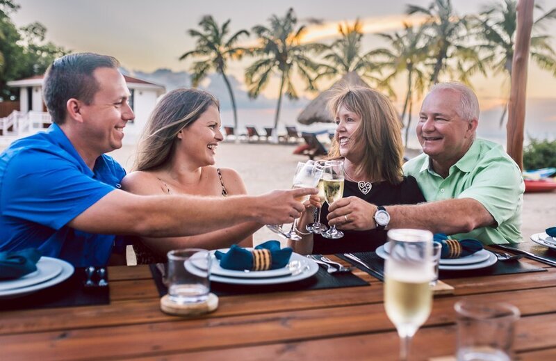 Smiling friends toast with glasses of champagne on a beach with palm trees