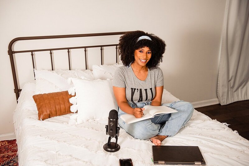 Truthfully Stew podcast host wearing a casual outfit sitting on a bed taking notes as she plans her next episode