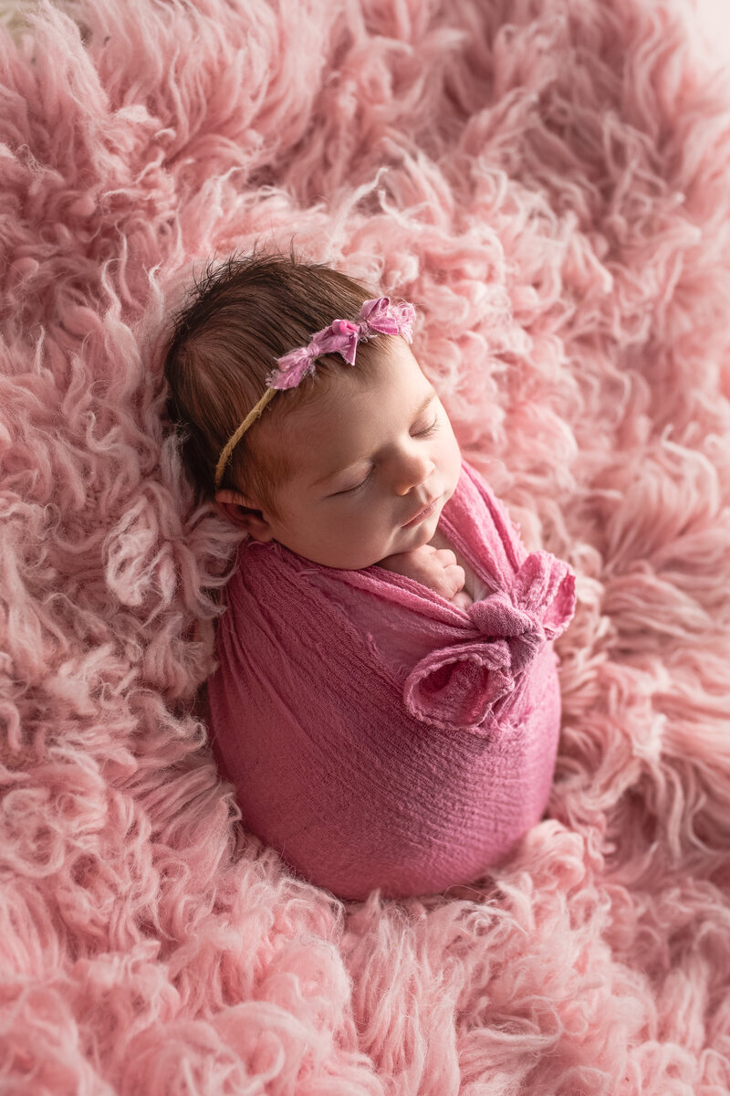 baby girl in a bright pink wrap on a light pink wool rug
