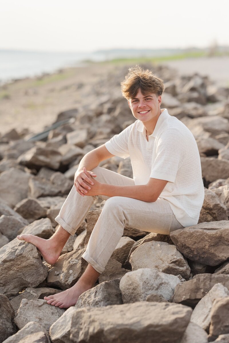 a boy in a white shirt and khakis posing on a rocky beach