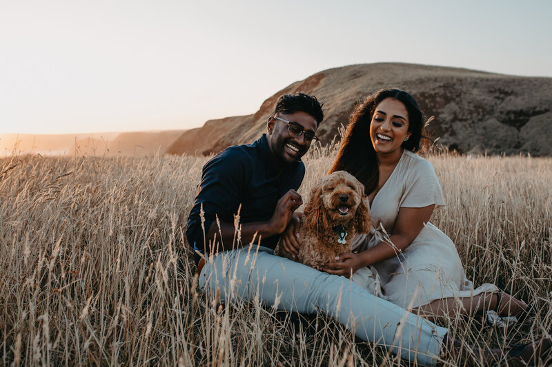 engagement session with dog sitting in the grass laughing