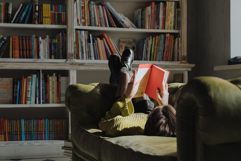 woman with her feet up on edge of couch reading a book
