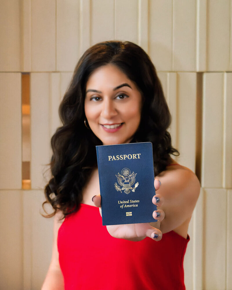 Sonia smiling in a red dress while holding up a US Passport