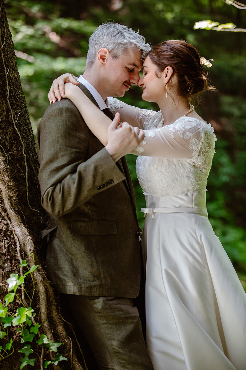 A couple is forehead to forehead surrounded by greenery.