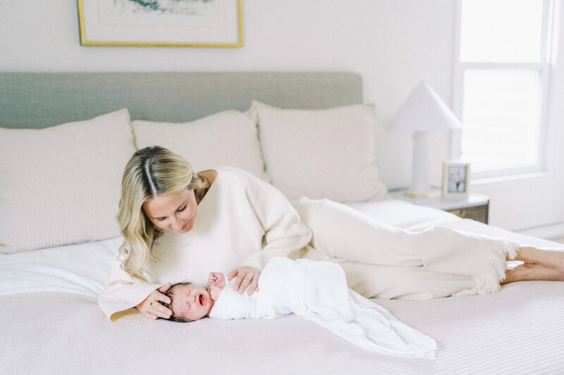 a mom watching her newborn baby lay on a bed