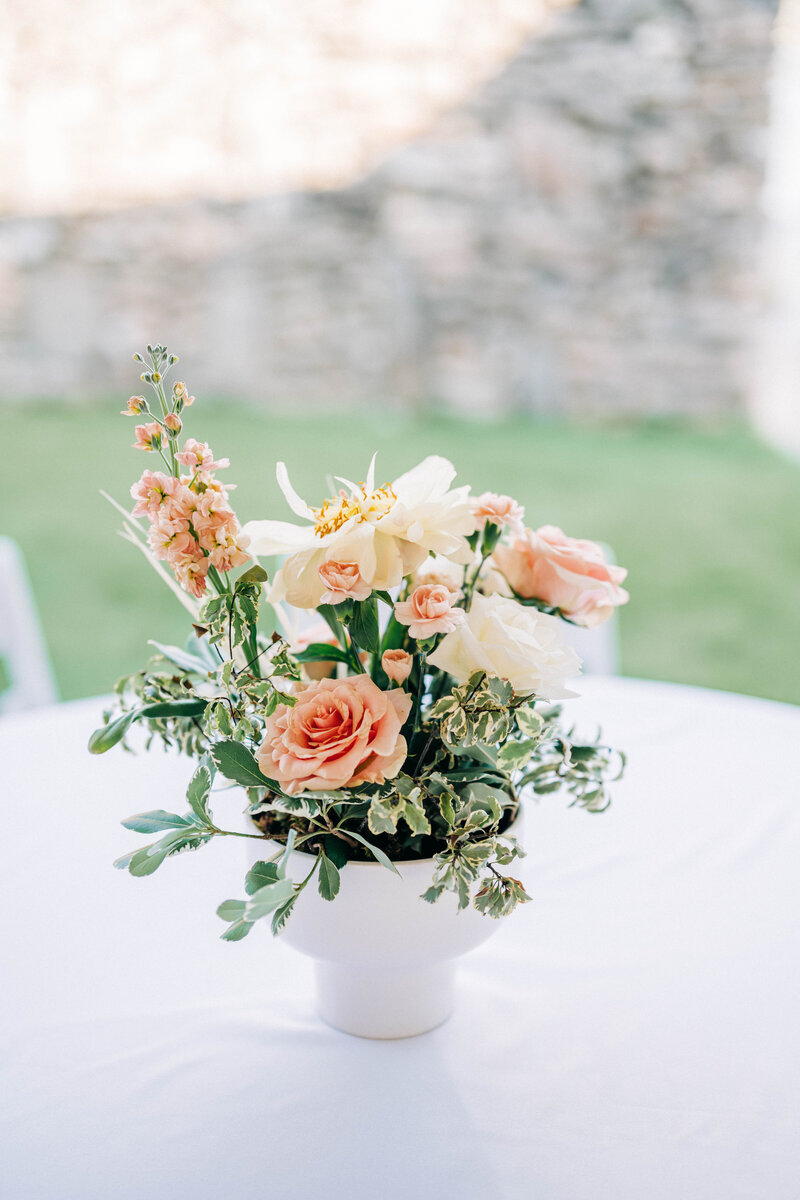 Peach floral centerpiece sitting on a white table in a white vase