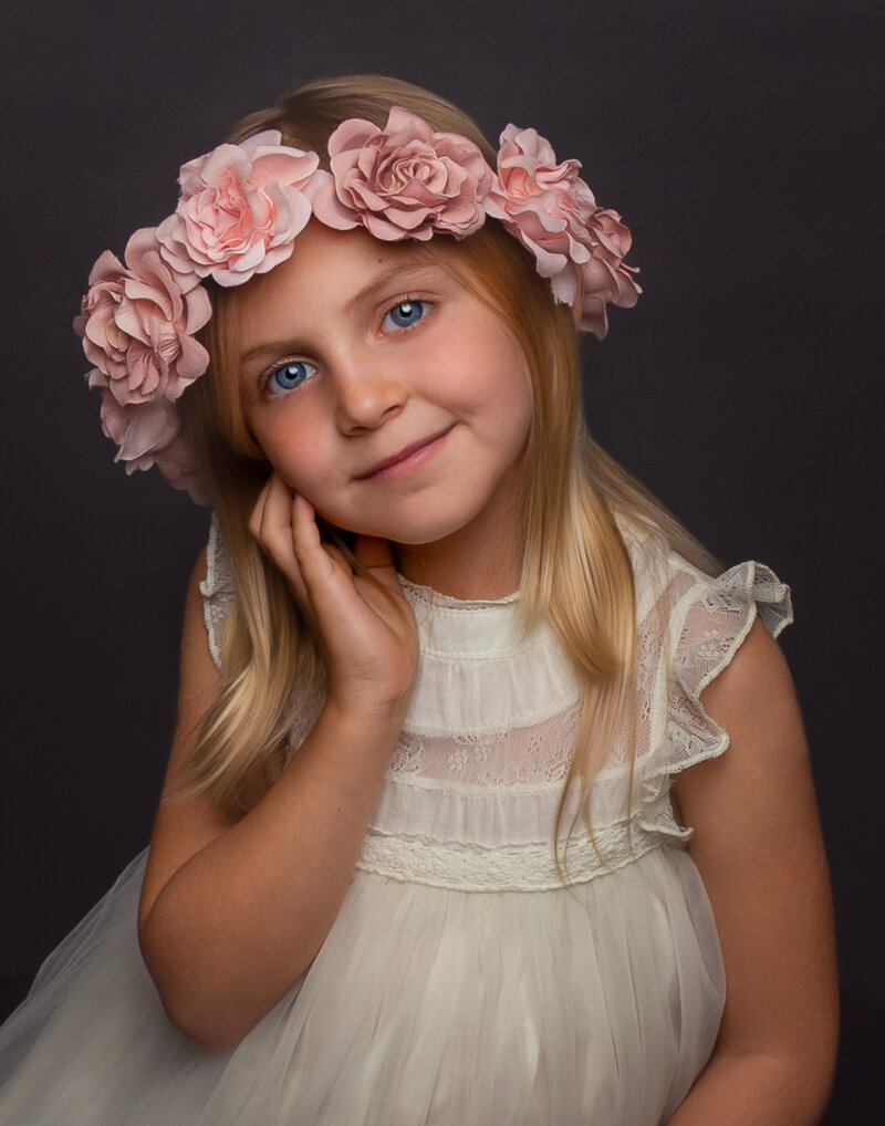 Smiling little girl with clear blue eyes and a crown of pale  peach colored flowers over her blonde hair
