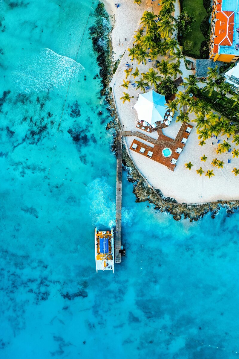 Top-down view of a tropical resort with palm trees, pool, and beach umbrellas