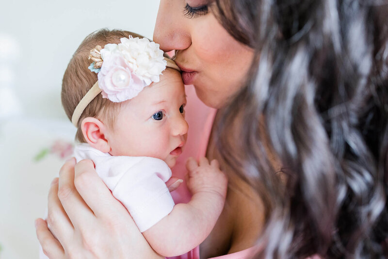 A close-up of a Haymarket newborn baby girl being kissed on the forehead by her mom.