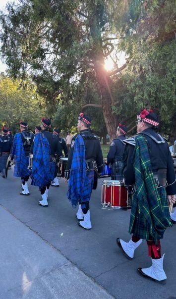 Members of Local 935 Pipes and Drums marching in uniform in the Annual California Firefighters Memorial Ceremony in Sacramento , carrying bagpipes and drums, with kilts and instruments visible from behind.