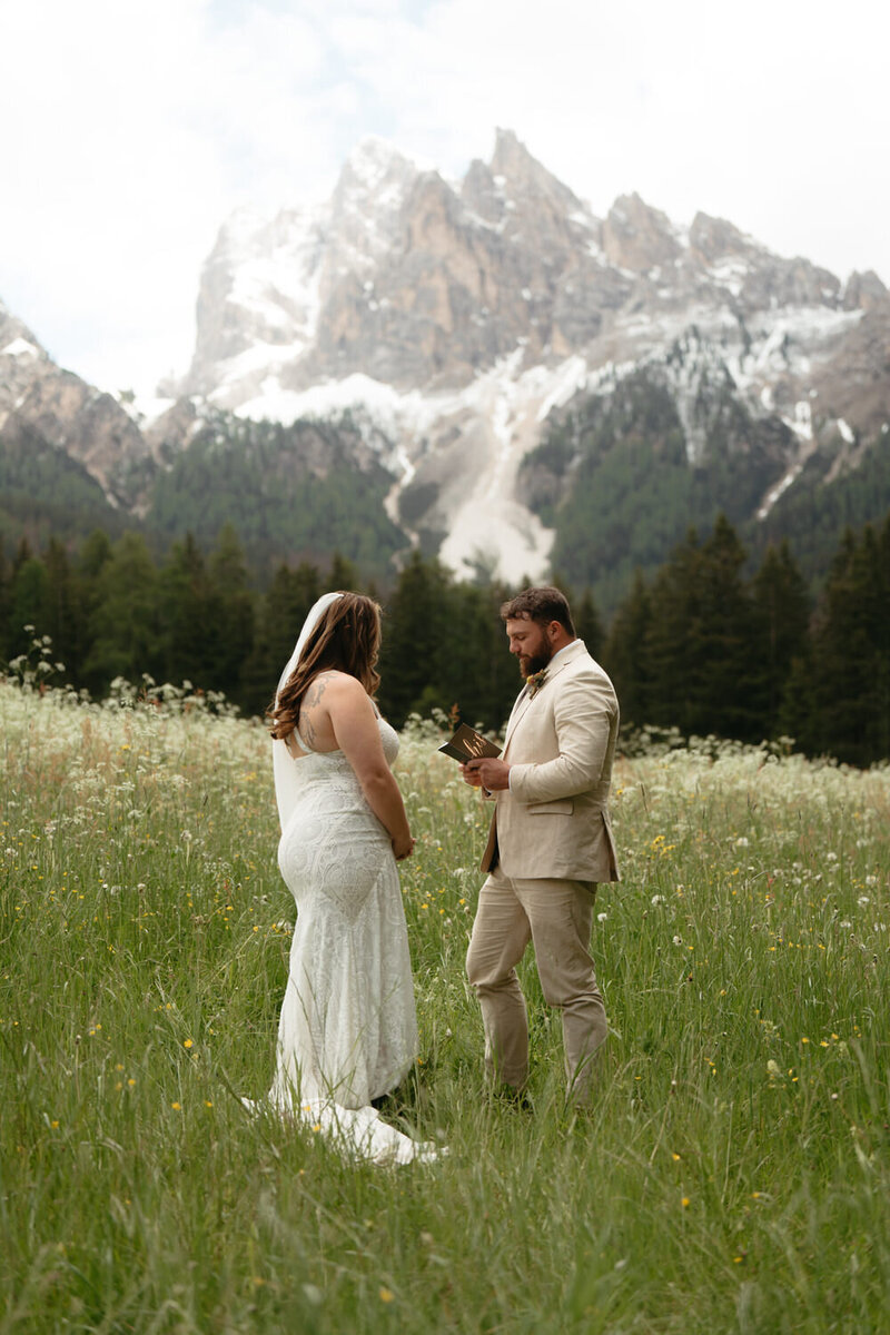 Groom reads vows to bride standing in a mountain meadow, a great Elopement Ceremony Idea