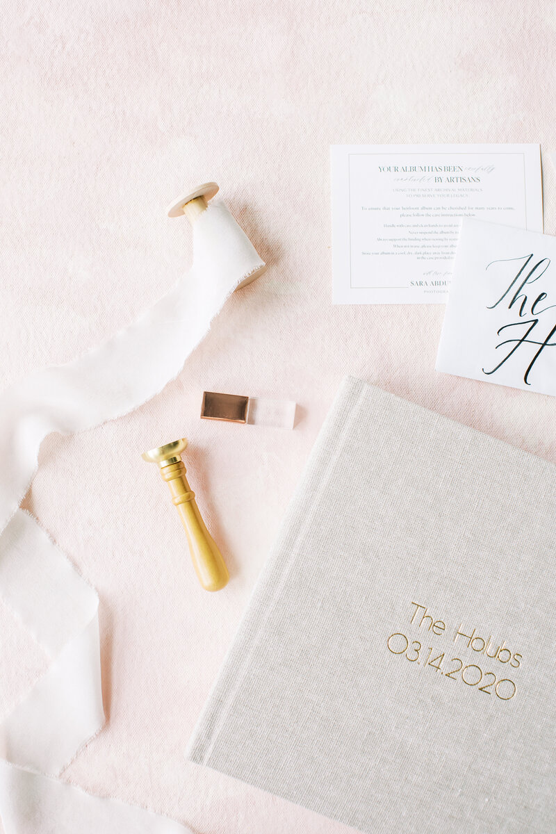 Wax seal and silk ribbon lay next to a rose gold crystal USB and wedding album