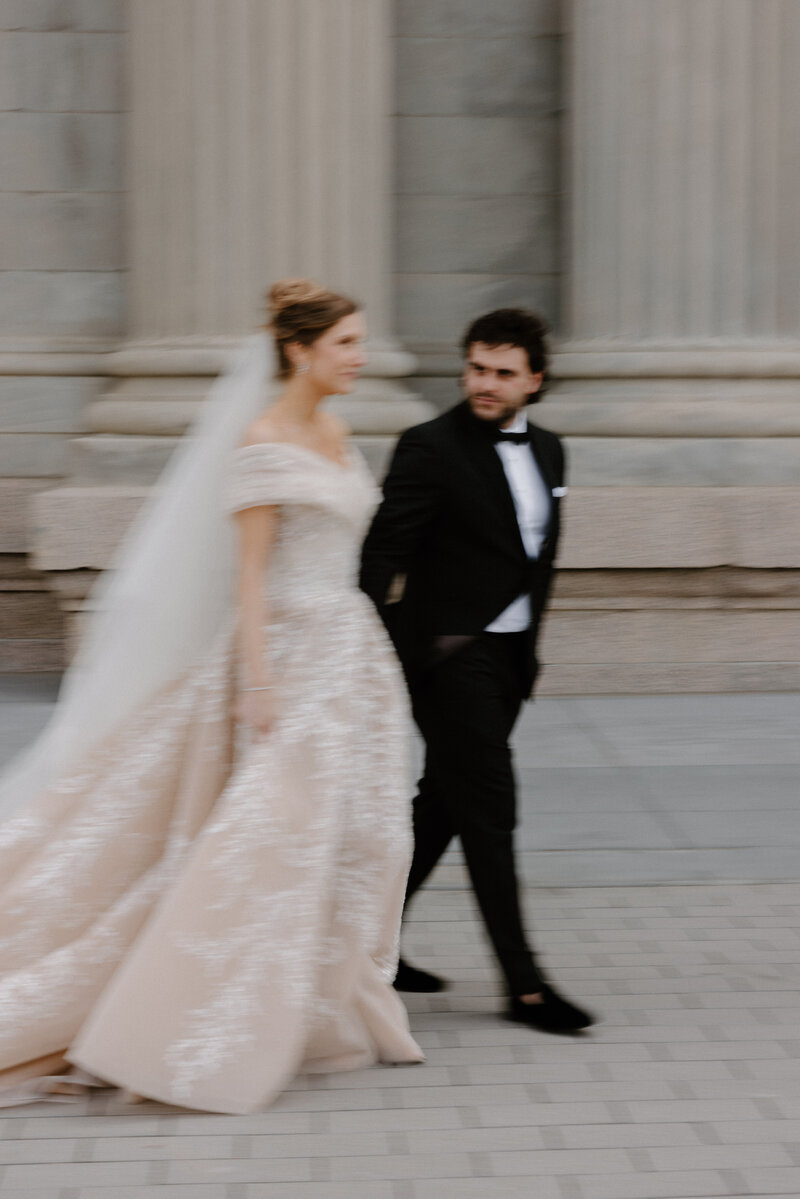 A slightly blurred image of a newlywed couple holding hands and walking together 