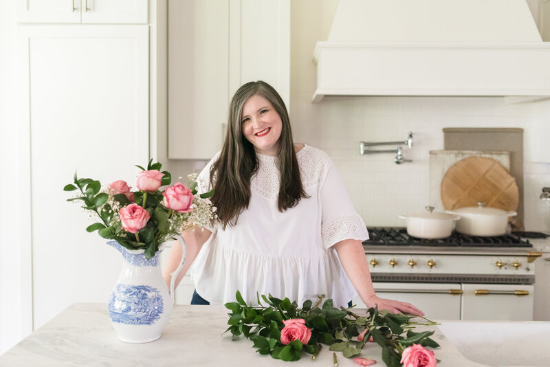 Lauren smiles at her kitchen island while arranging pink roses in a vase
