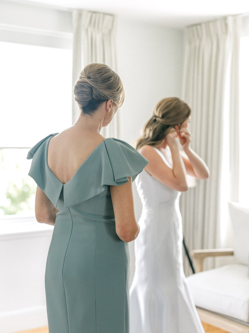 Mom looking at bride while she puts on her wedding earrings
