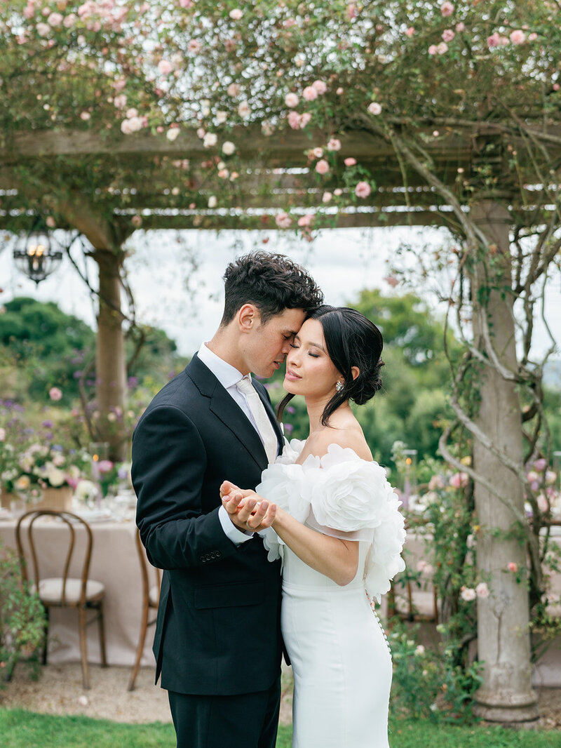 Bride and groom holding hands under a trellis covered in flowers