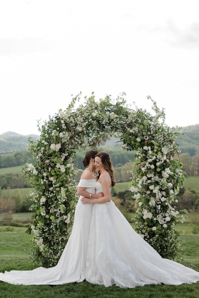 two brides embrace under a large floral arch