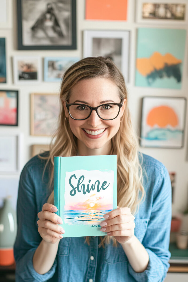 A personal branding image of a woman with long blonde hair and glasses smiling and holding a book that says Shine.