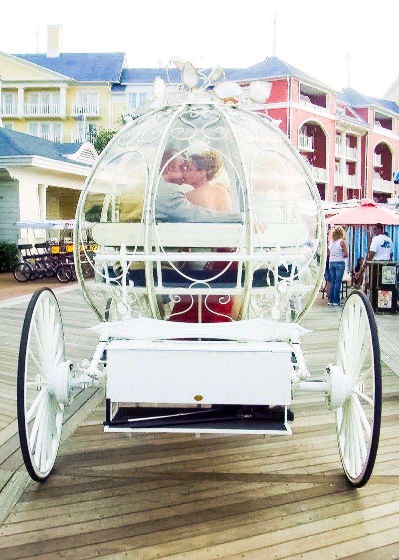 A married couple riding in the Cinderella Glass Carriage on their Disney Vow Renewal day in front of the Boardwalk Resort.