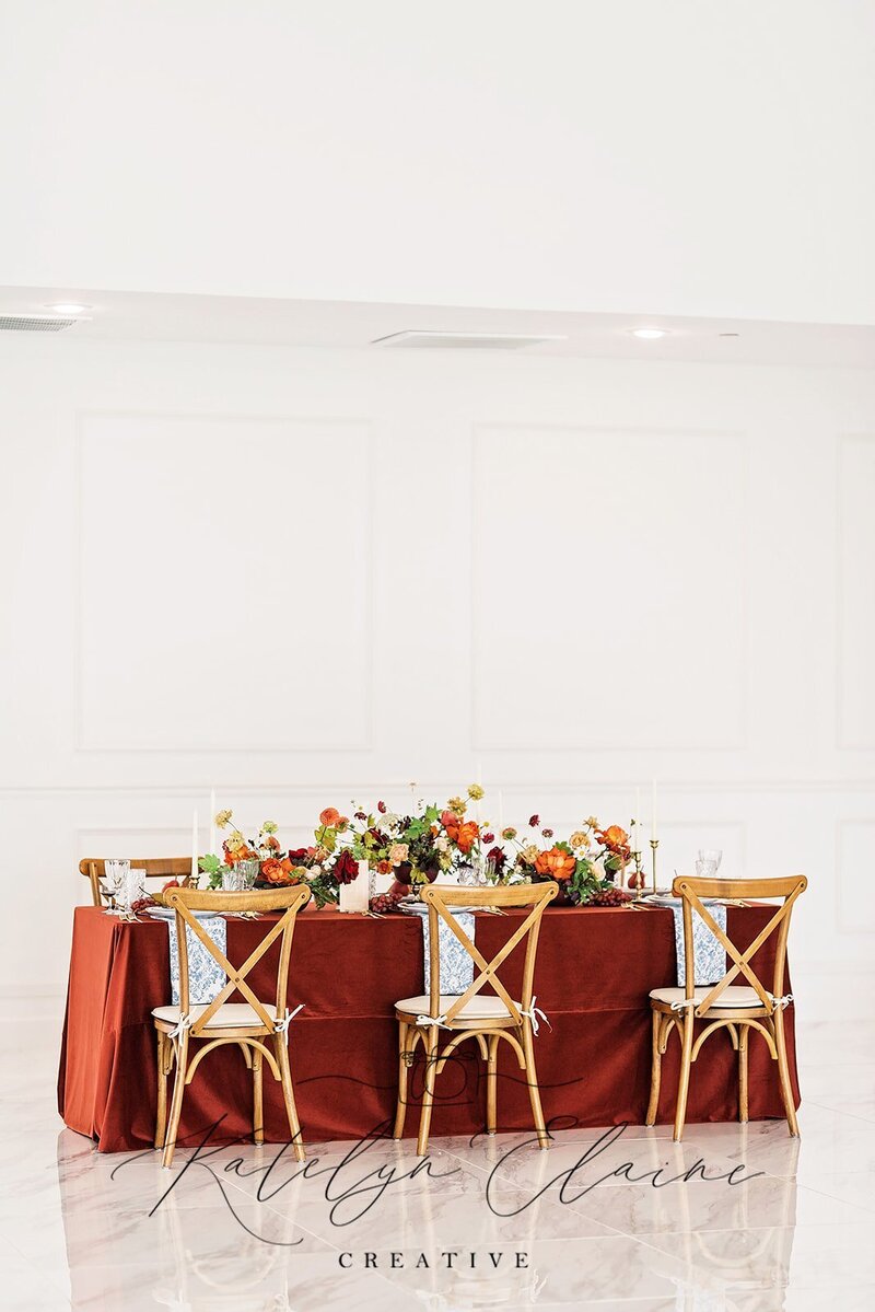 Crossback chairs with rust-colored linens and vibrant autumn centerpiece at an elegant indoor reception table.