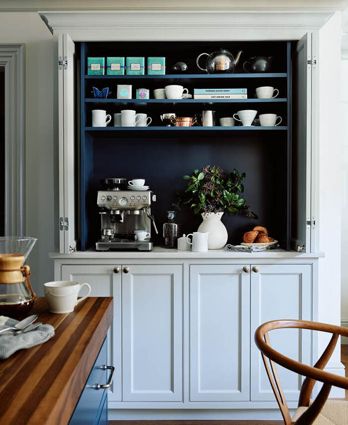 Custom cabinets in light grey with navy interiors house a coffee station for espresso, kettle, and mugs, blending style and function in a brownstone kitchen.