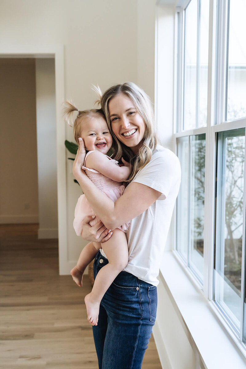 Wellness coach and holistic nutritionist Erica Taylor smiling and holding her toddler, promoting realistic wellness for moms in early motherhood