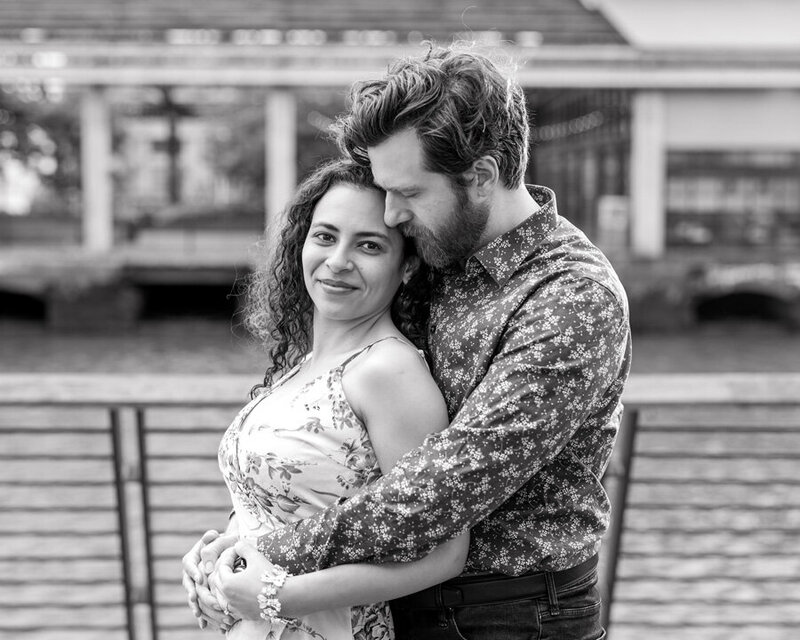 Black and white photo of a couple snuggling at Race Street Pier, capturing a timeless and intimate engagement moment.