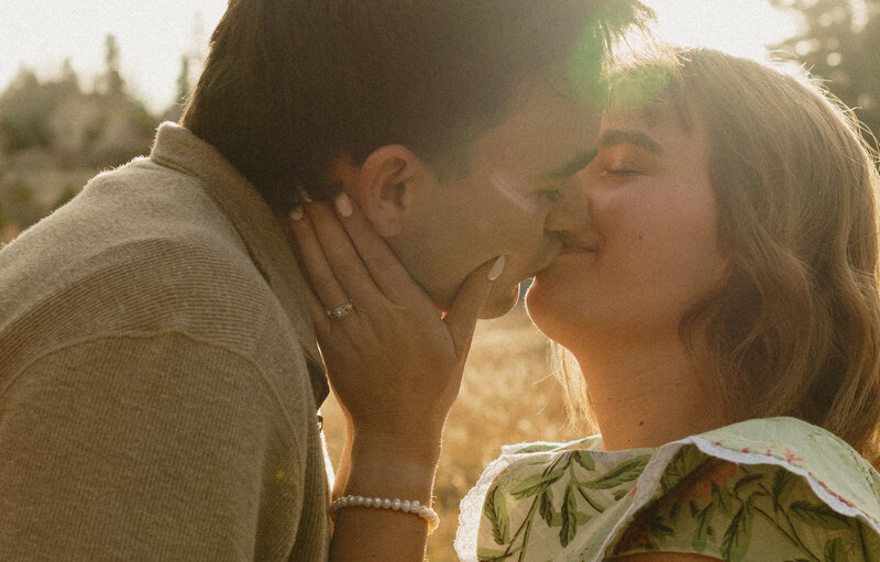 A slightly blurry photo of an engaged couple walking towards each other. They are outdoors with tall greenery framing them.