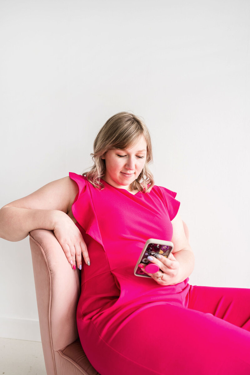 Kat Murphy in a pink jumpsuit sitting in a pink chair looking at her phone