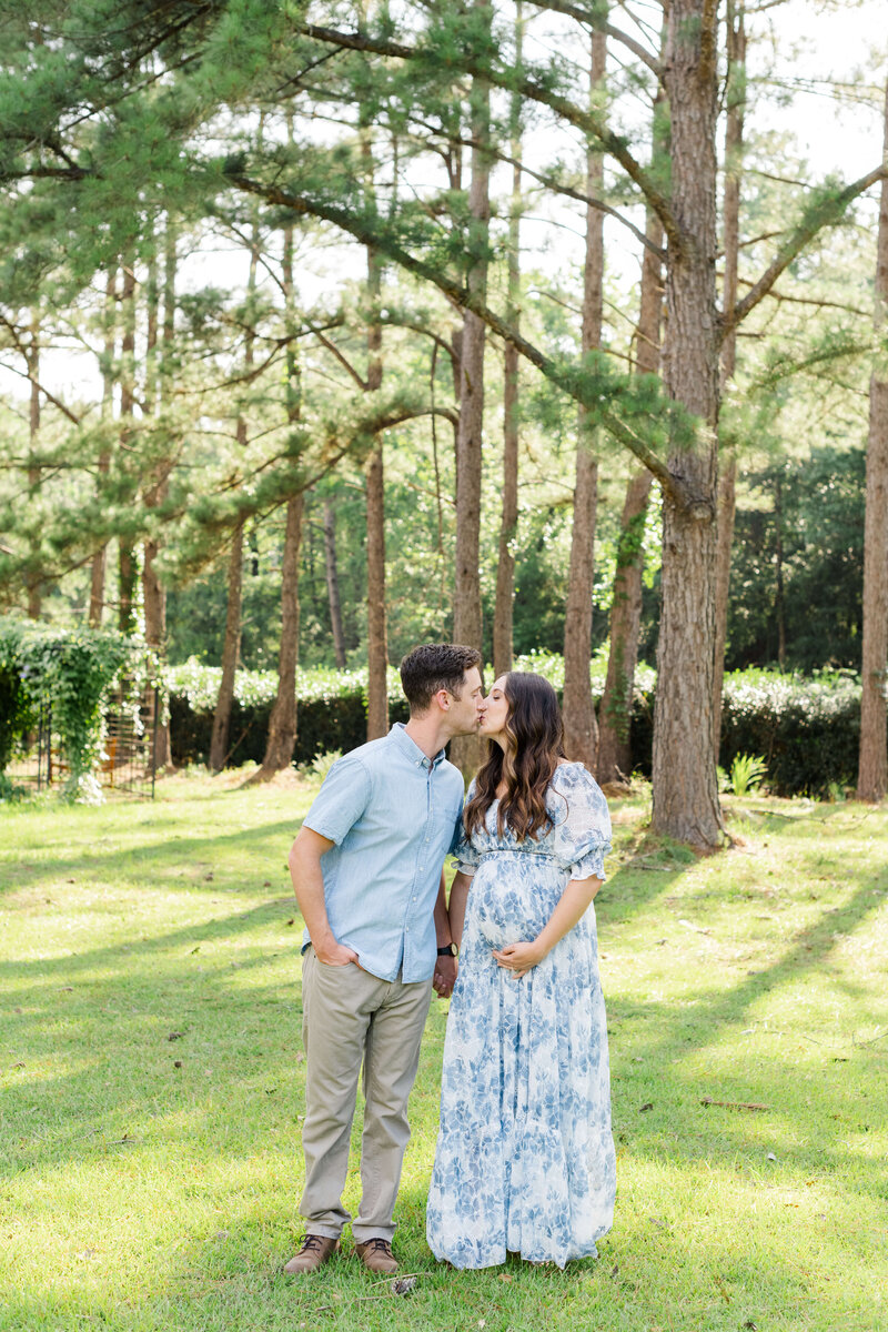 Man and woman kissing while holding pregnant belly in dothan alabama woods for maternity photography session