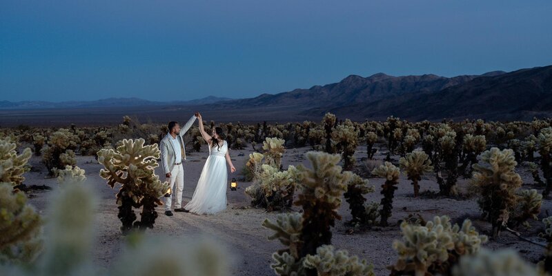 Couple dancing during their Joshua Tree elopement at blue hour, surrounded by cholla cactus garden and desert mountains.