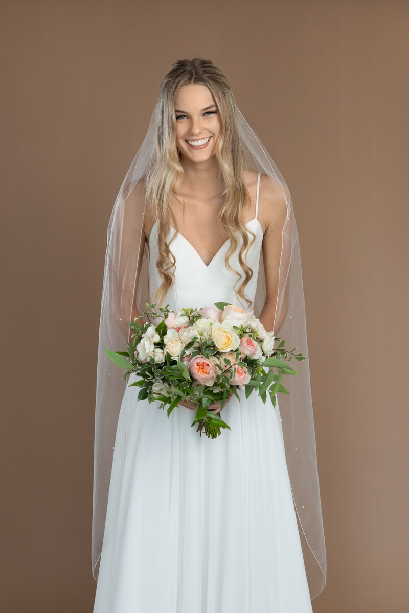 Bride wearing a waltz length veil with pearls and serged edge and holding a white and blush bouquet