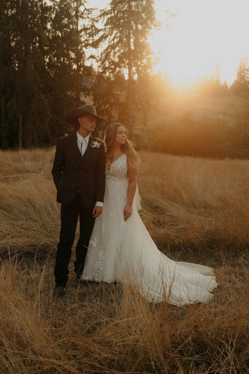 A couple standing in a golden field at sunset, the bride in a flowing dress