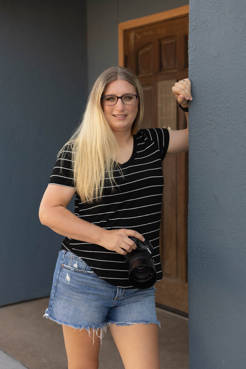 Megan standing near a doorway holding her camera with a confident stance | Senior Photographer in Lawrence, KS