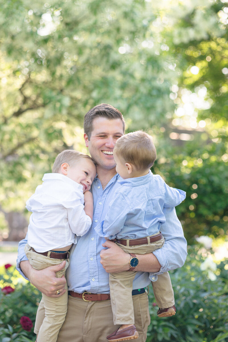 Dad holding his two sons and smiling in a beautiful Louisville Kentucky  garden during their family photo session