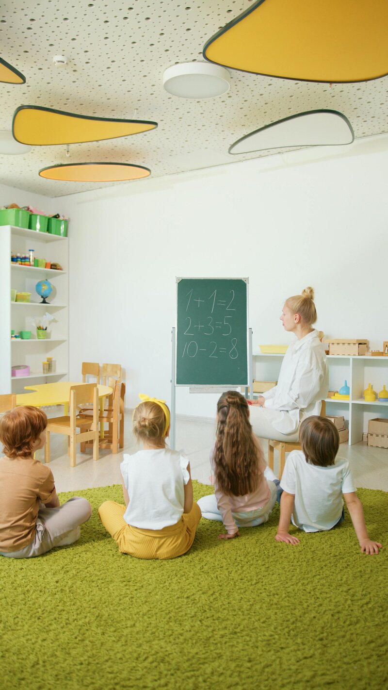 childrean in classroom sitting on floor in front of chalk board