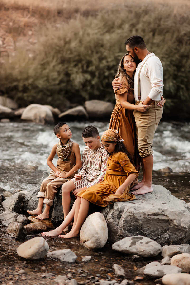 3 children sitting on rock together near stream in front of their parents standing behind them at Viestenz-Smith Mountain Park Colorado