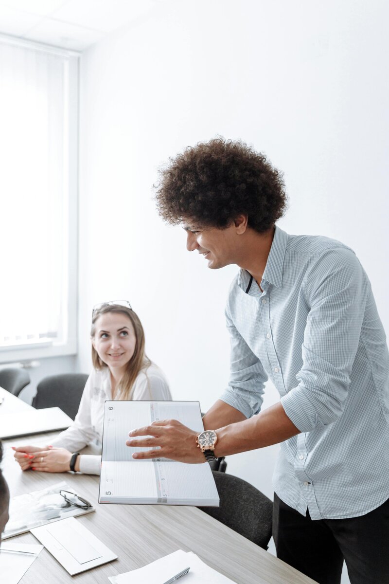 Professional man with curly hair smiling while working at laptop, wearing light blue striped shirt, representing focused leadership.